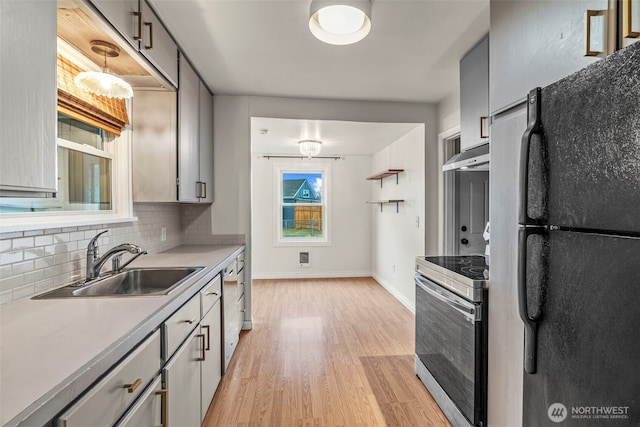 kitchen with stainless steel electric stove, freestanding refrigerator, a sink, under cabinet range hood, and backsplash