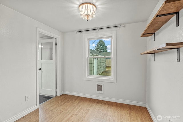 spare room with baseboards, light wood-style floors, and a chandelier