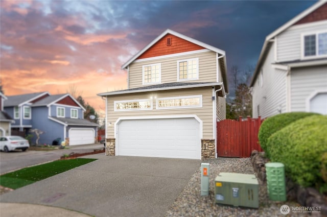 view of front of home with stone siding, concrete driveway, an attached garage, and fence