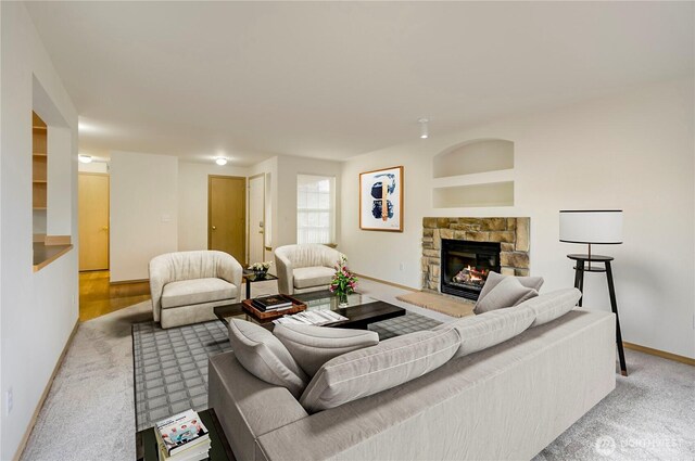 living area with a stone fireplace, light colored carpet, and baseboards