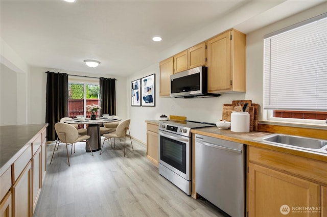 kitchen with light wood finished floors, recessed lighting, a sink, light brown cabinetry, and stainless steel appliances