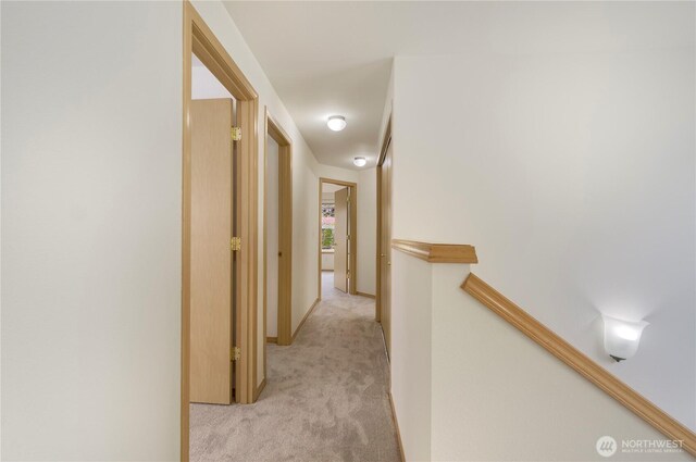 corridor featuring an upstairs landing, baseboards, and light carpet