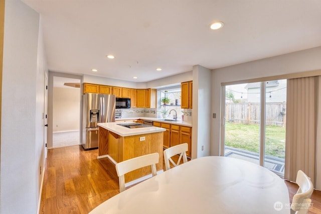 kitchen featuring light wood-style flooring, stainless steel refrigerator with ice dispenser, a sink, black microwave, and light countertops