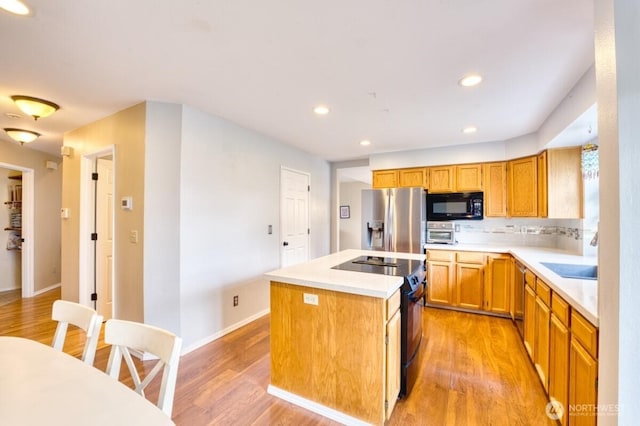 kitchen with a kitchen island, light wood-style flooring, a sink, black appliances, and light countertops