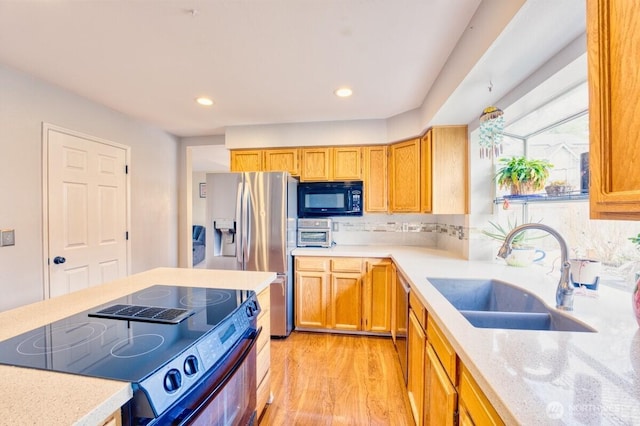 kitchen featuring light wood finished floors, light stone countertops, decorative backsplash, black appliances, and a sink