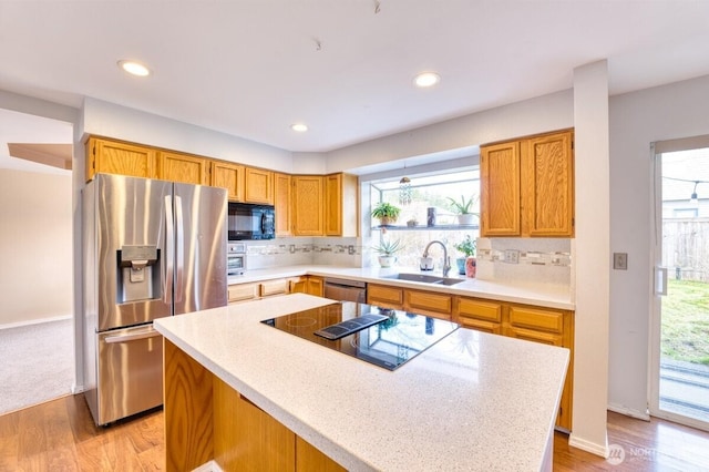 kitchen with black appliances, a sink, backsplash, a center island, and light countertops