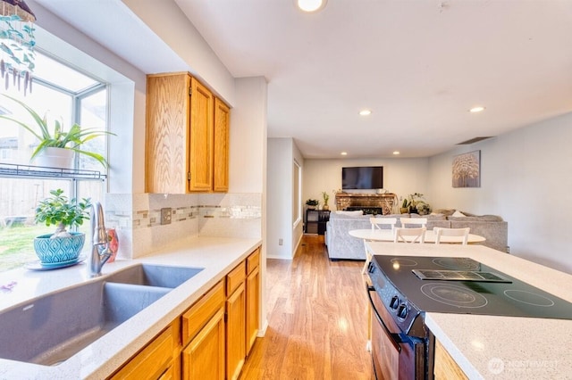 kitchen with backsplash, stainless steel electric range oven, a fireplace, light wood-style floors, and a sink