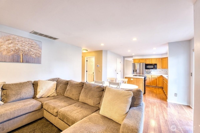 living area with recessed lighting, visible vents, and light wood finished floors