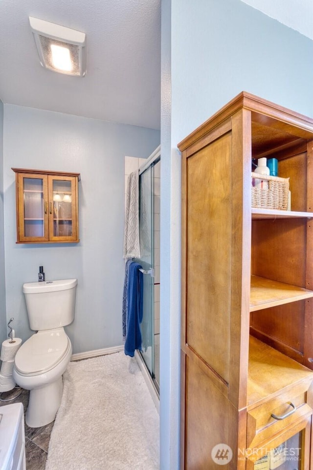 bathroom featuring toilet, baseboards, and a stall shower