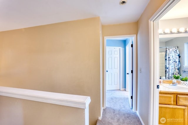 hallway with light colored carpet, baseboards, and a sink