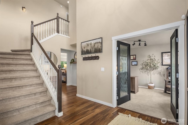 interior space with baseboards, track lighting, wood finished floors, and a towering ceiling