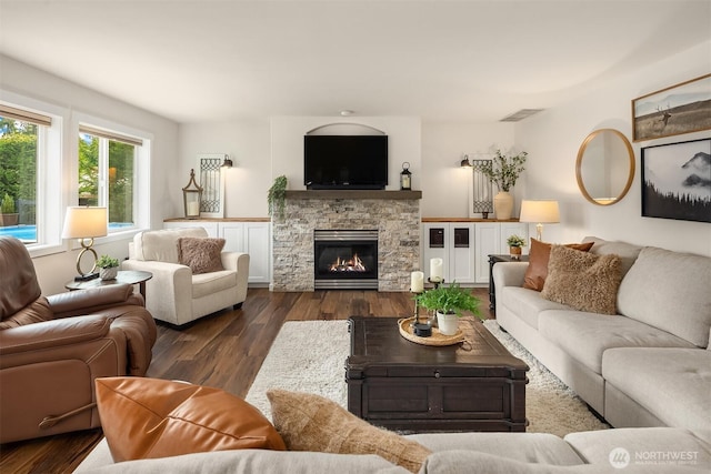 living room featuring a stone fireplace, visible vents, and dark wood-style flooring