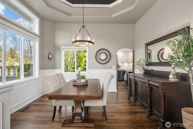 dining space featuring arched walkways, plenty of natural light, wainscoting, and dark wood-type flooring