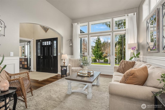 living room with arched walkways, a wainscoted wall, vaulted ceiling, and wood finished floors