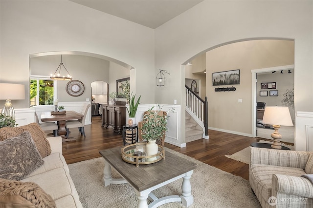 living room with a chandelier, a wainscoted wall, wood finished floors, and stairway