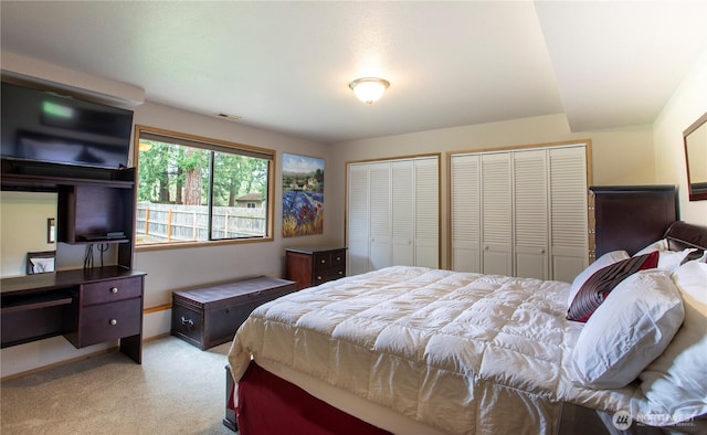 bedroom featuring light colored carpet, two closets, and visible vents