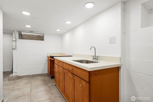 kitchen with concrete block wall, brown cabinetry, recessed lighting, a sink, and light countertops