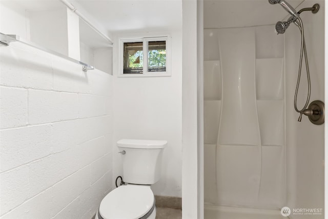 bathroom with concrete block wall, toilet, and a shower