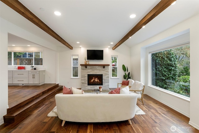 living area featuring recessed lighting, a warm lit fireplace, baseboards, and wood finished floors