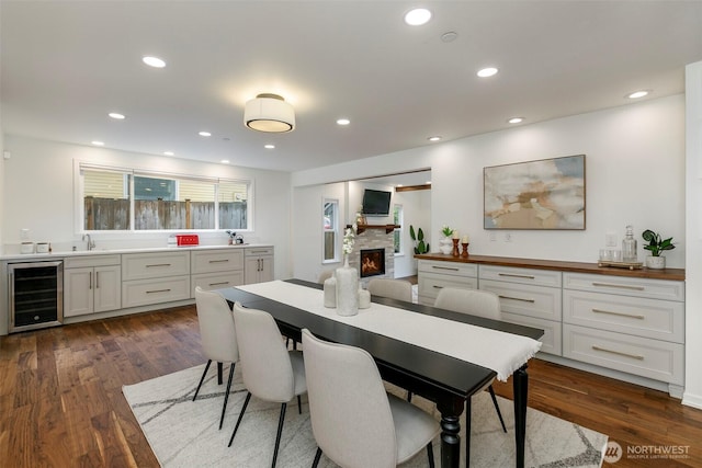 dining room with a fireplace, dark wood-type flooring, recessed lighting, and beverage cooler