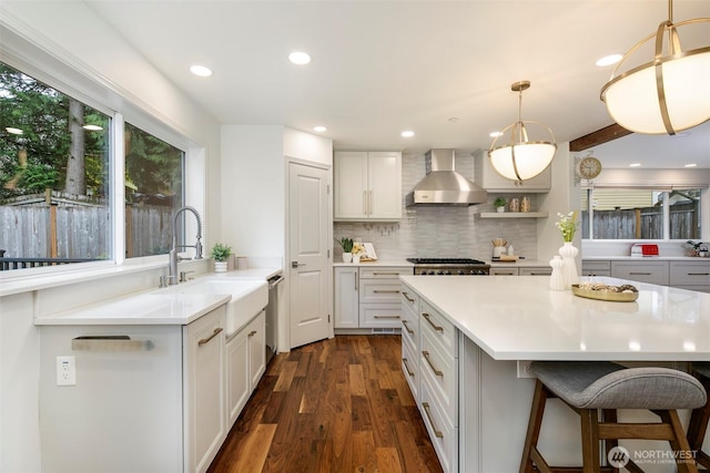 kitchen with a sink, wall chimney range hood, dark wood-style floors, light countertops, and dishwasher