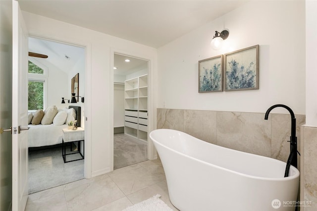 full bath featuring a walk in closet, lofted ceiling, a soaking tub, and ensuite bath