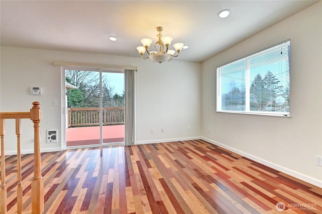 spare room featuring a notable chandelier, wood finished floors, and baseboards