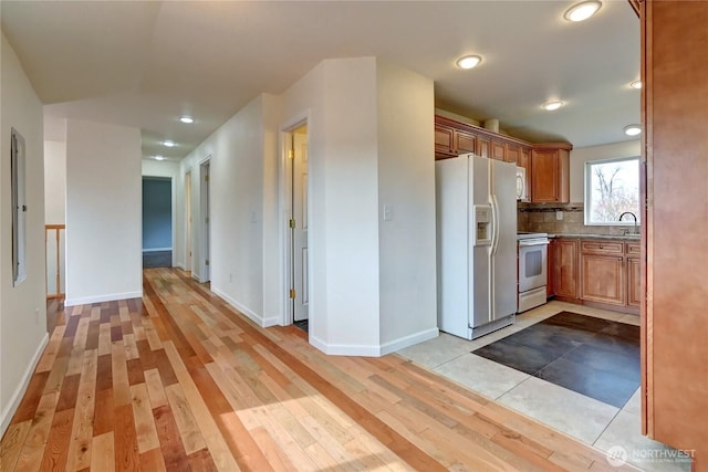 kitchen with backsplash, baseboards, light wood-style flooring, brown cabinets, and white appliances