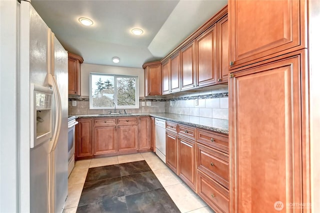 kitchen with tasteful backsplash, brown cabinets, white appliances, stone countertops, and a sink