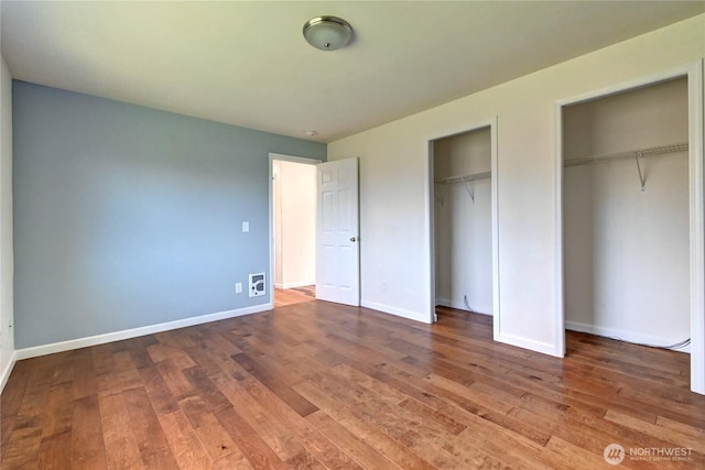 unfurnished bedroom with baseboards, two closets, and wood finished floors