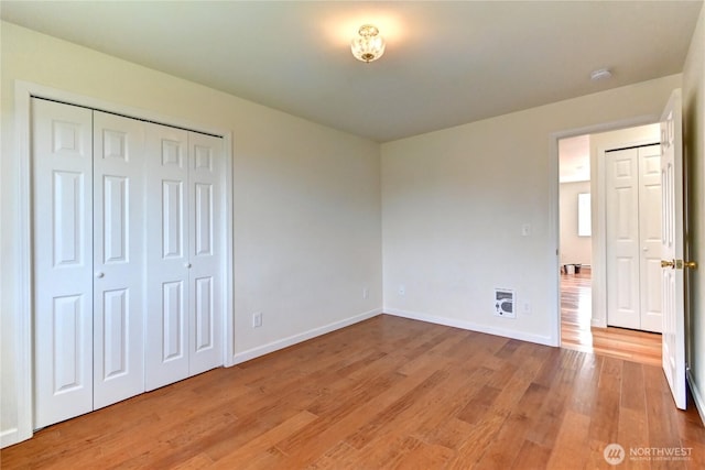 unfurnished bedroom with heating unit, light wood-style flooring, a closet, and baseboards