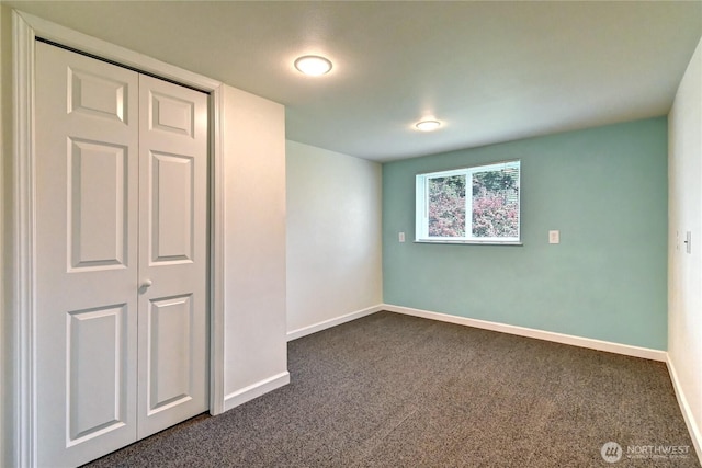 unfurnished bedroom with dark colored carpet, a closet, and baseboards