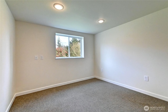 unfurnished room with baseboards and dark carpet