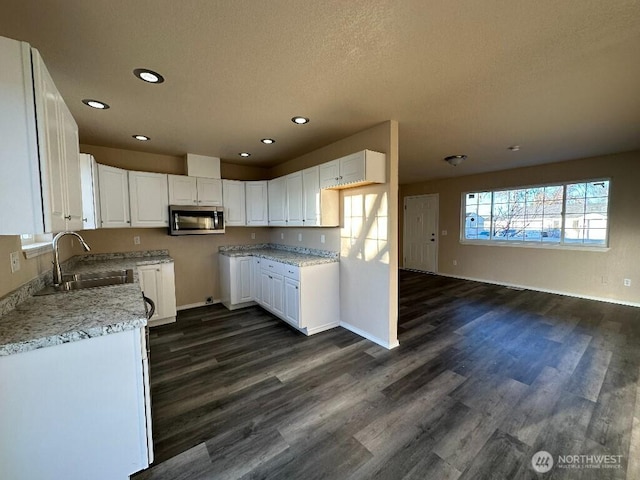 kitchen featuring a sink, stainless steel microwave, dark wood-style floors, and white cabinets