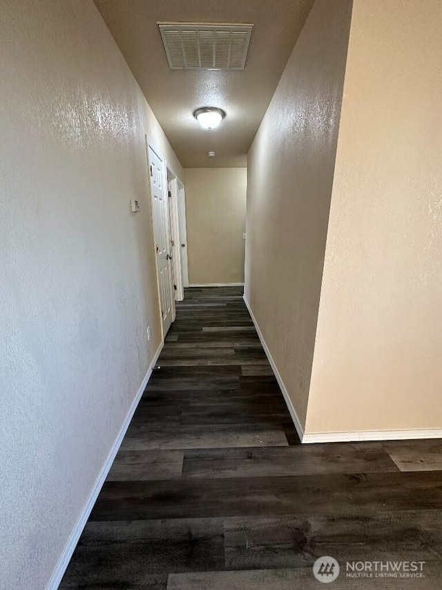 hallway featuring wood finished floors, visible vents, a textured wall, and baseboards