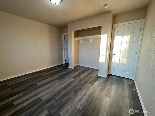 unfurnished bedroom featuring a textured ceiling, dark wood-style floors, a closet, and baseboards