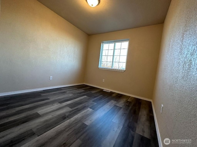 empty room featuring baseboards, dark wood-style floors, vaulted ceiling, and a textured wall