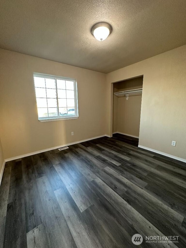 unfurnished bedroom with visible vents, a textured ceiling, a closet, baseboards, and dark wood-style flooring