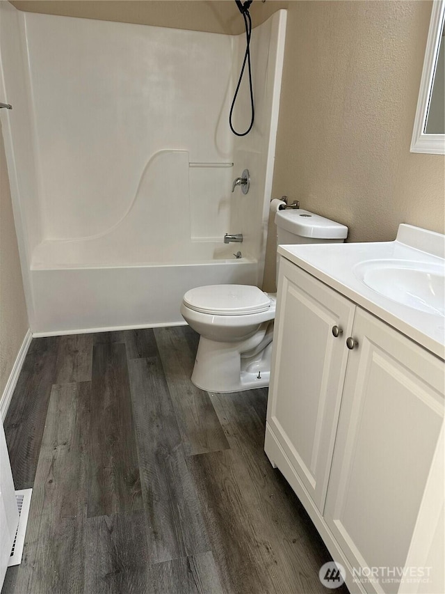 bathroom with toilet, shower / bathtub combination, wood finished floors, vanity, and a textured wall