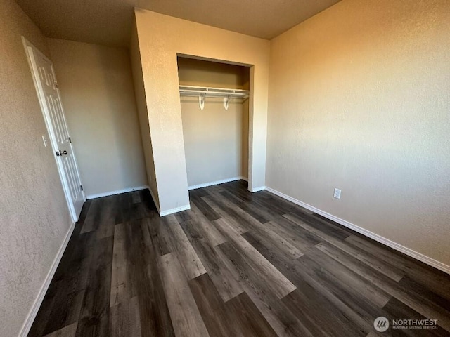 unfurnished bedroom with a closet, baseboards, and dark wood-style flooring