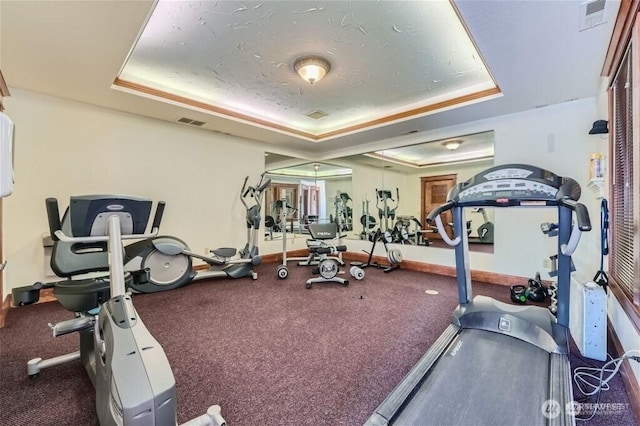 exercise room with a raised ceiling, baseboards, and visible vents