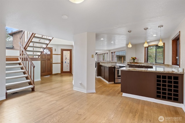 kitchen featuring stainless steel electric range oven, baseboards, light wood-style flooring, a sink, and hanging light fixtures