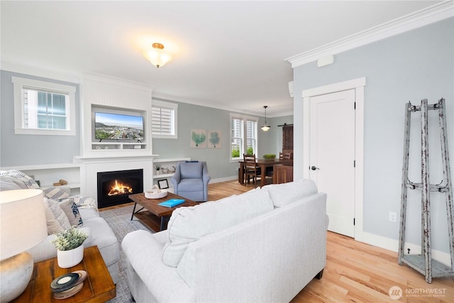 living area with baseboards, a large fireplace, crown molding, and light wood finished floors