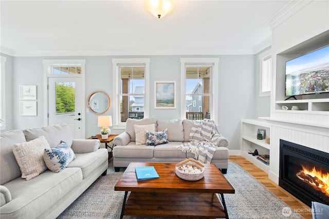 living room with a fireplace with flush hearth, built in features, crown molding, light wood finished floors, and baseboards