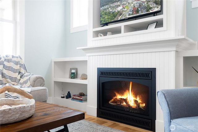 sitting room featuring built in features, a warm lit fireplace, and wood finished floors