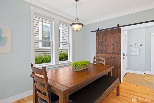 dining area featuring light wood-style flooring, a barn door, baseboards, and ornamental molding