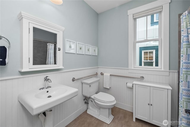 full bathroom featuring a wainscoted wall and toilet