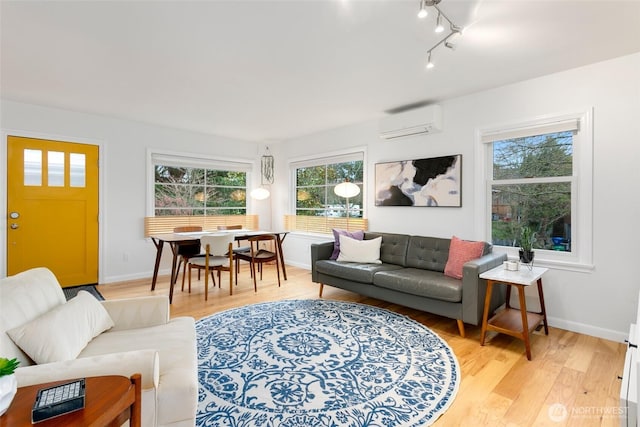 living area featuring track lighting, light wood-style flooring, a wall mounted air conditioner, and baseboards