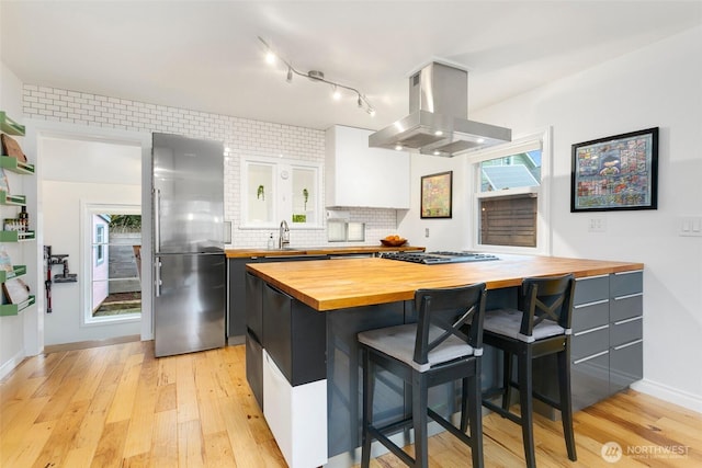 kitchen featuring butcher block countertops, a breakfast bar, tasteful backsplash, island range hood, and high end refrigerator