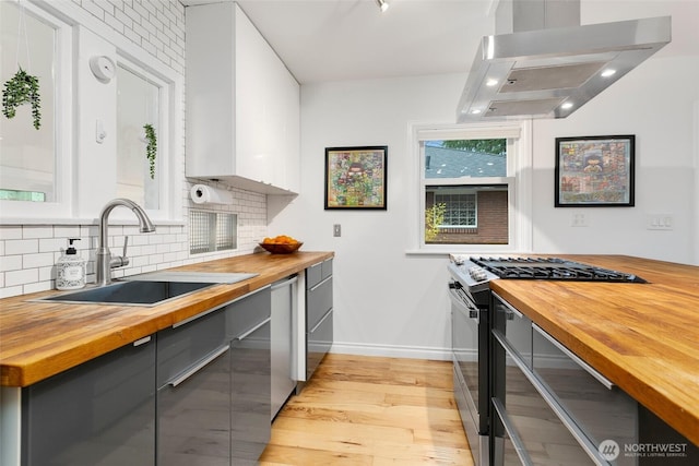 kitchen with wall chimney range hood, gray cabinetry, appliances with stainless steel finishes, and butcher block counters